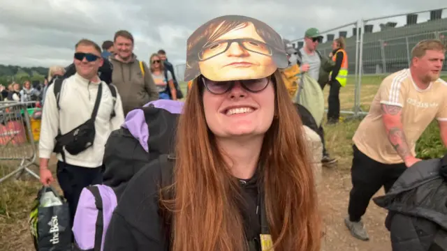 A woman with a Jarvis Cocker mask on her head