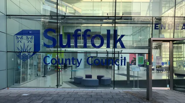 A view of the entrance into Suffolk County Council's headquarters. It is a glass building with the county council's name and logo on the front.