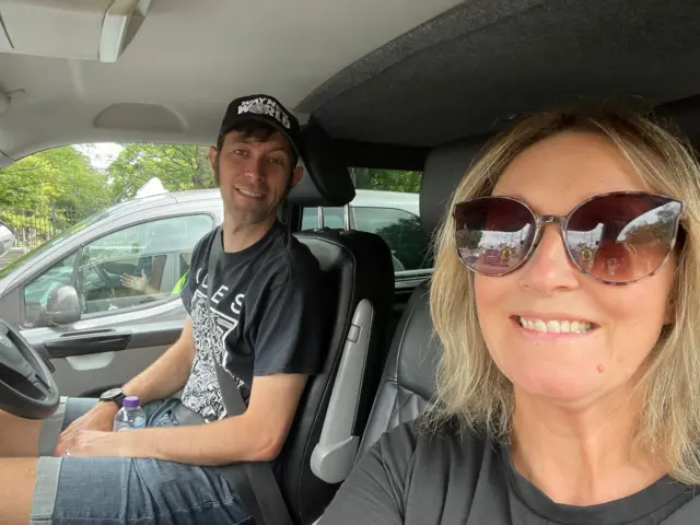 Two people sat in a car smiling at the camera
