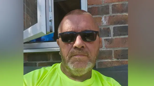 A selfie of Martin Wegg. He is wearing sunglasses and a florescent green top. He has shaved hair and a beard.