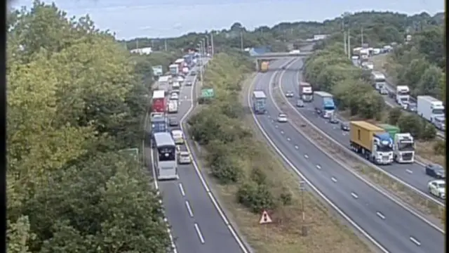 A traffic camera view of the Copdock Interchange. The slip roads up to a roundabout are filled with vehicles. The main carriageway has some traffic on it.
