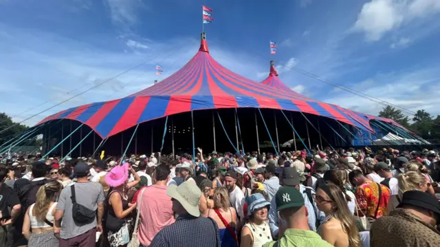 A crowd gathers outside a red and blue striped tent