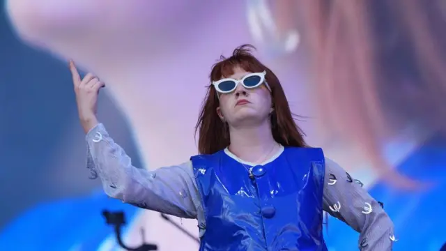 CMAT on the stage, holding up one arm as she dances
