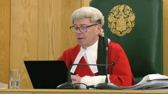 Judge Mr Justice Bennathan sits and delivers remarks in a white wig