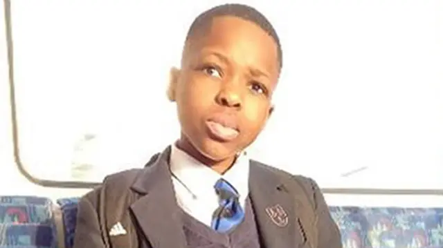 Danio Anjorin is sat on a Tube carriage looking towards a camera while wearing his school uniform and a black addidas backpack