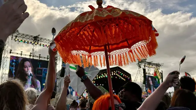 A view over the top of heads in the audience at Morissette's set, where a couple of fans hold silver spoons aloft