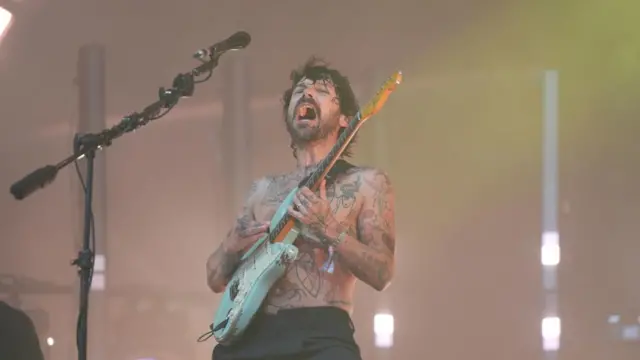 Biffy Clyro baş şarkıcısı Simon Neil geri eğilir ve ana sahnede bir gitar tutarken gömleğiyle şarkı söyler
