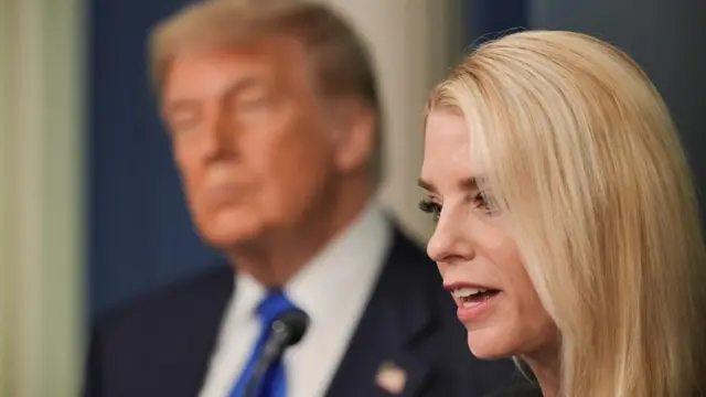Pam Bondi is seen from the side profile, she has blonde, long hair. Trump is seen in the background.