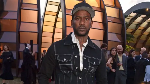 Skepta wearing a matching denim jacket and hat and posing for the camera