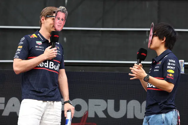 Max Verstappen and Yuki Tsunoda speaking on stage at the Austrian Grand Prix while wearing Brad Pitt masks