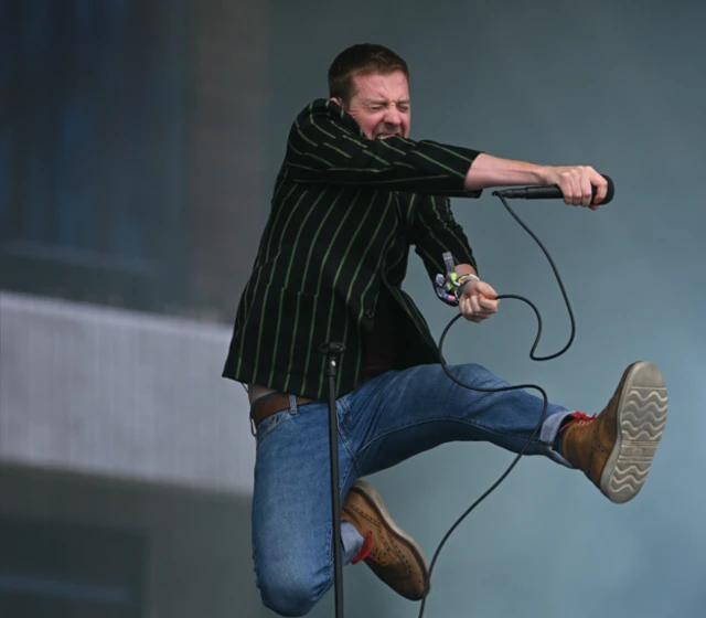 Ricky WIlson jumps in the air clutching a mic while singing
