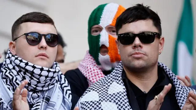 Irish rap group Kneecap singer, Liam O'Hanna (L), who performs under the stage name Mo Chara, stands with band mates Naoise O Caireallain, aka Moglai Bap (R) and JJ O'Dochartaigh aka DJ Provai (C), outside Westminster Magistrates' Court