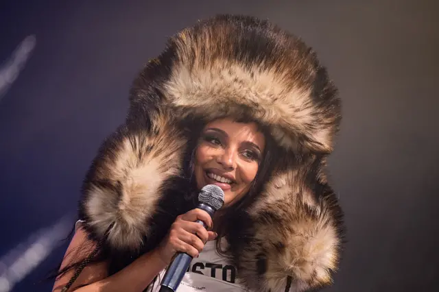 JADE wearing a huge furry hat with earflaps while singing on stage