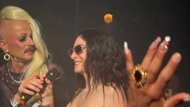 Lorde wearing a strapless top decorated with buttons and singing into a microphone