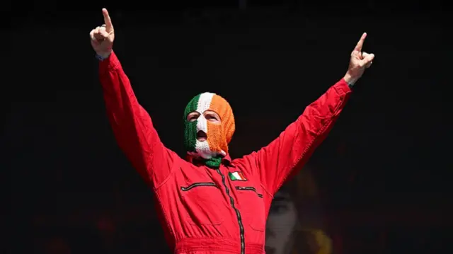 DJ Provaí on the stage at Glastonbury wearing a red boiler suit and a balaclava in the colours of the Irish flag