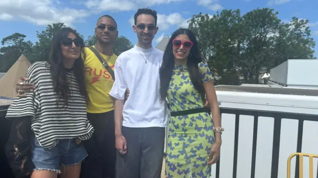 A group of four people wearing sunglasses pose for a photo