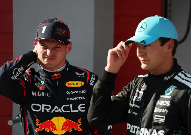 Max Verstappen scrunches up his face while stood next to George Russell, who is adjusting his cap, at the Emilia-Romagna Grand Prix at Imola in May 2025