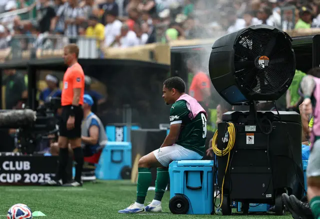 Roque sits in front of a huge fan with a wet towel on his shoulders