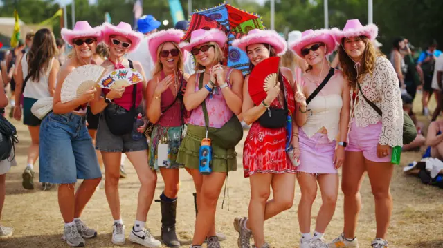 Seven female festivalgoers standing in a line facing the camera. There are all wearing pink cowboy hats