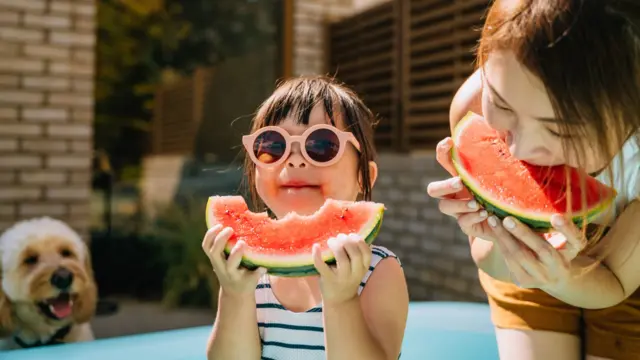 A little girl with sunglasses eating fresh ripe watermelon with her mother