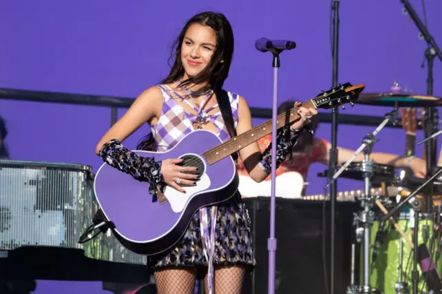 Olivia Rodrigo performing at Glastonbury in 2022 wearing a purple outfit and holding a purple guitar.
