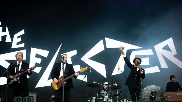 Black backdrop with the selecter written is white jagged letters. Band all wearing black suits and ties and white shirts
