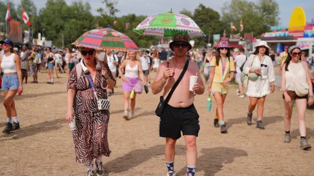 A shirtless man and a woman in a dress each shading themselves with bright printed parasols