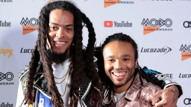 Bobby Vylan stands with his arm around Bobbie Vylan, smiling against a Mobo Awards backdrop