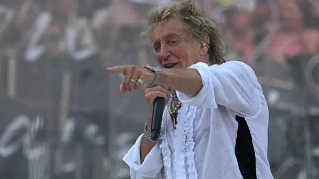Rod Stewart points to the crowd as he sings into a mic