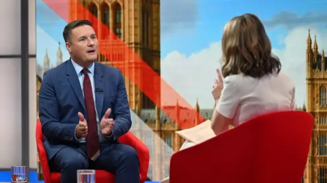 Wes Streeting in suit and tie talking to Victoria Derbyshire, seen here from behind, on the set of Sunday with Laura K
