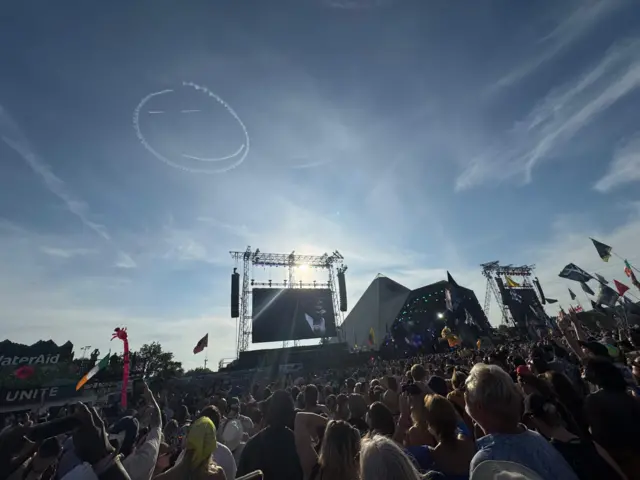 a smiley face drawn by a plane in the sky above the pyramid stage