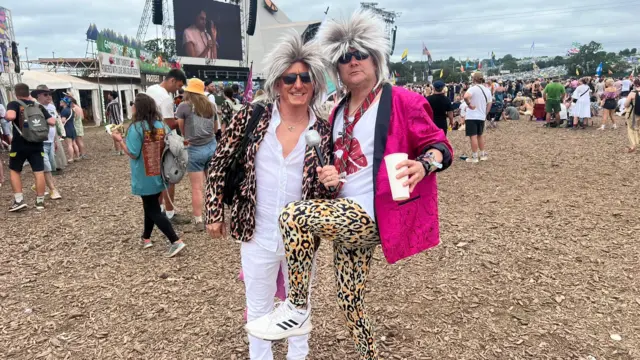 Rob Divall, wearing a white shirt and pants with a cheetah print blazer, and Coman Wakefield, who is donning cheetah print pants and a pink blazer. Both are wearing a spikey white hair wig and sunglasses.