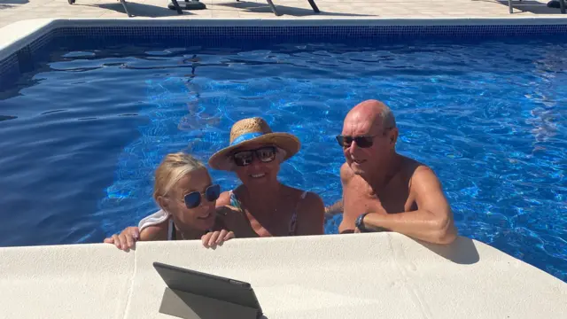 Three people in a swimming pool watching the set on an iPad