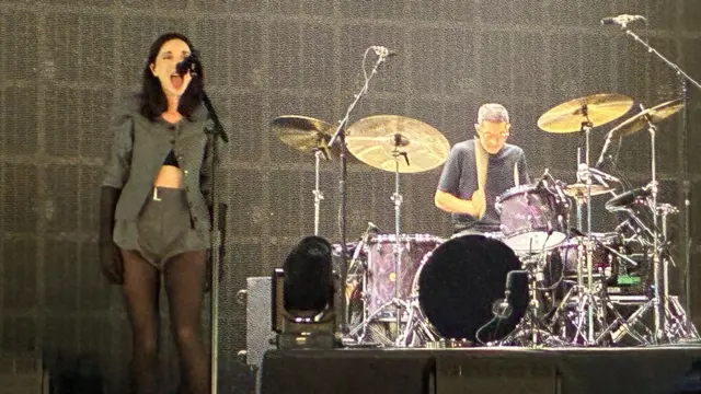 St Vincent standing on the left of the image. There is a drumkit being played on the right.