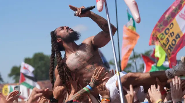 One of the members of Bob Vylan crowd surfs with his top out