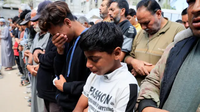 A line of mourners, many of whom are in tears, bow their heads