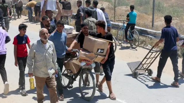 The image focuses on a group of men walking towards the camera. Boxes of aid have been loaded onto a bicycle which they are steering