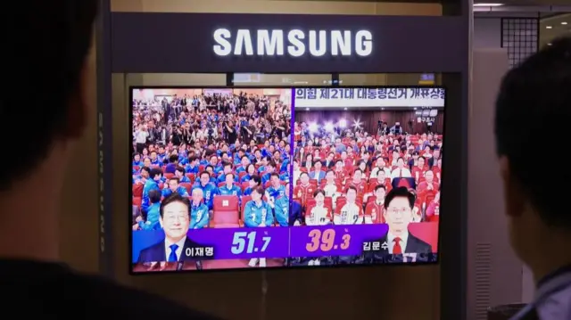 People watch a TV report at Seoul Station, where an exit poll projects that Lee Jae-myung will win the election with 51.7% of the votes