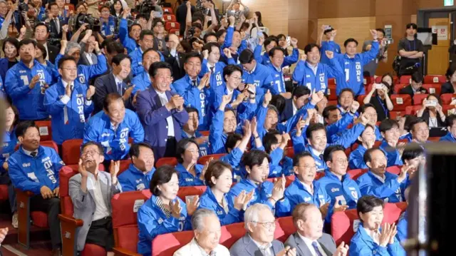 People at Lee's headquarter stand up, waving their arms, with smiles on their faces