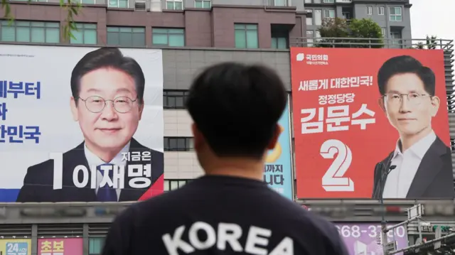 A man looks up at large posters of the two main candidates in South Korea's 2025 presidential election, Lee Jae-myung and Kim Moon-soo.