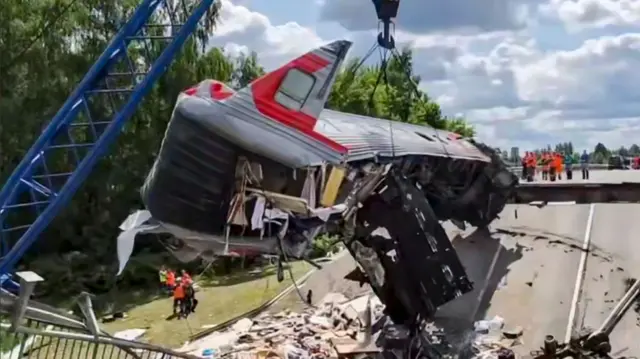Debris of derailed train removed off collapsed concrete bridge in Russia. Emergency operators visible in orange hi-vis in the bottom left of the snap