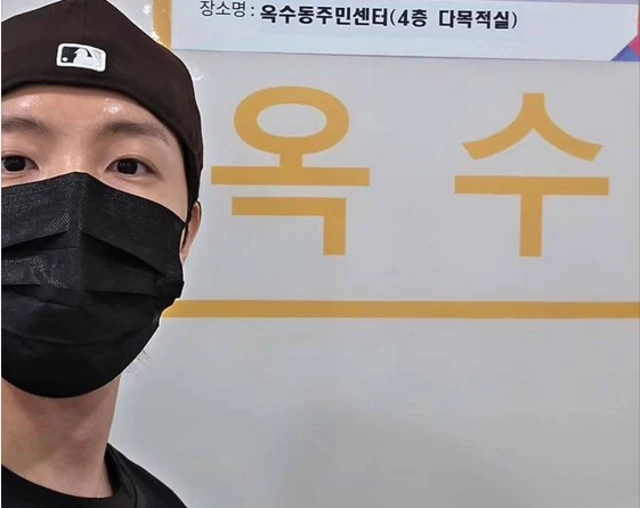J-Hope wearing a black hat and a black face mask, posing in front of a polling booth