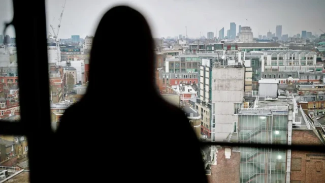 A woman's silhouette as she looks through a window towards a city skyline