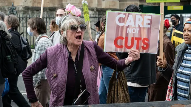 A woman holds a sign that reads care not cuts