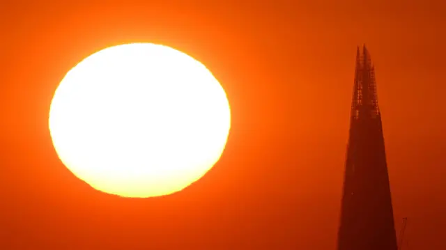 The Sun rises behind the Shard skyscraper in London with an orange sky in the background