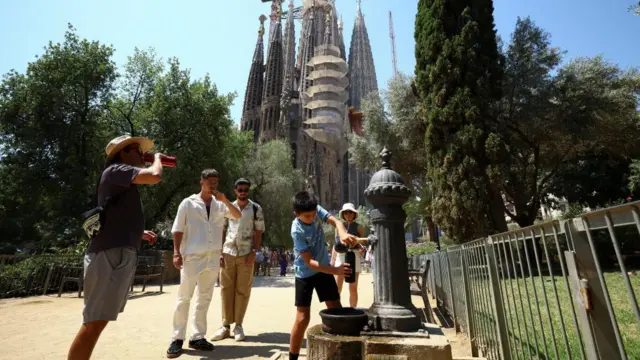 People fill up their bottles from a fountain next to Sagrada Familia Basilica in Barcelona