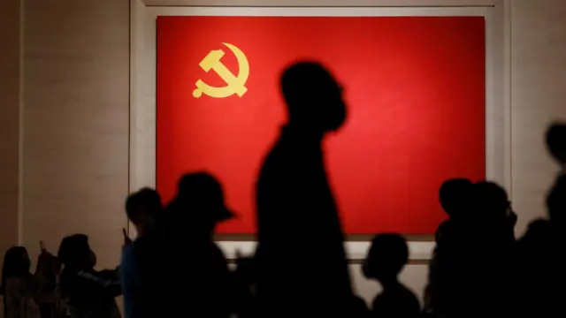 Visitors to the Museum of the Communist Party of China in Beijing are silhouetted against the flag of the Chinese Communist Party