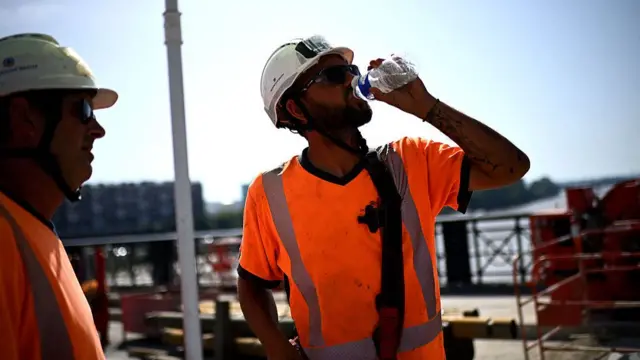 A man drinks water to cool down as he works on the reinforcement site of the Pont de pierre during a heatwave in Bordeaux