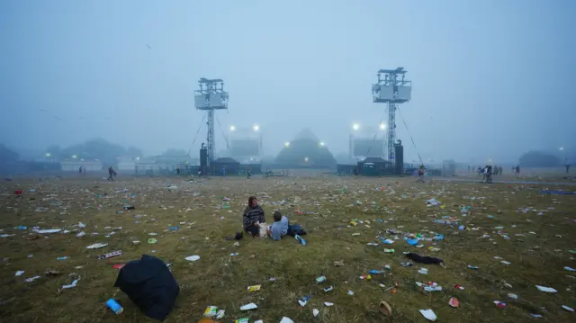 The last of the festivalgoers sit in a field covered in litter on a misty morning at the end of the Glastonbury Festival at Worthy Farm in Somerset. Picture date: Monday June 30, 2025