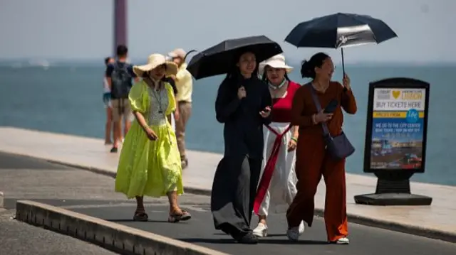 A group of women wear hats and hold umbrellas to shield themselves from the scorching sun during the first heatwave of the year in Lisbon